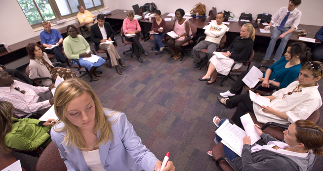 This is a classroom of students sitting in a circle with the teacher writing on the board.